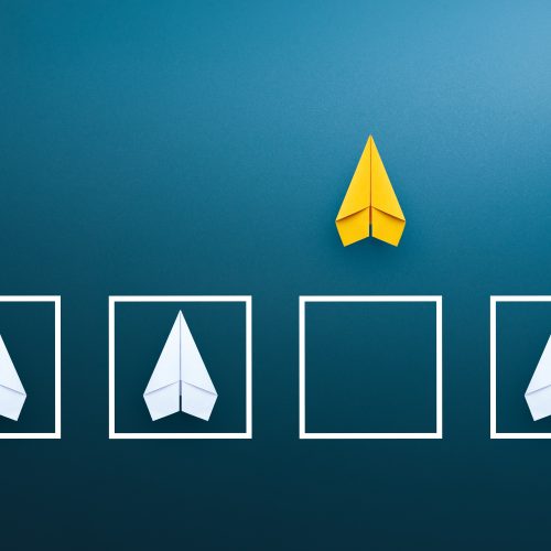 Image of a yellow paper plane outside of a box alongside three plain paper planes inside boxes to demonstrate diversity of thought